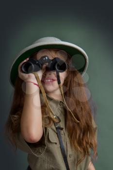 little girl in tropical uniform and cork helmet looks through binoculars