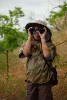 a little girl in a tropical khaki uniform and a cork with binoculars looking for adventures in nature