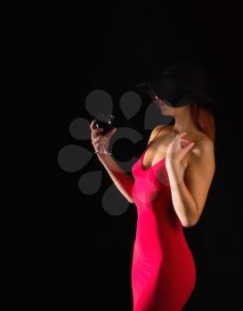 sensual girl in a bright red dress and black wide-brimmed hat stands with a glass of wine on a dark background