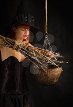 sexy girl dressed as a medieval witch with a broom in her hand conjures over a cauldron