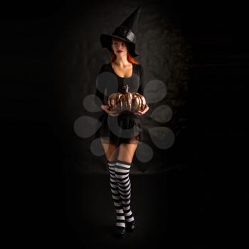 sexy girl dressed as a medieval witch stands with a pumpkin in their hands