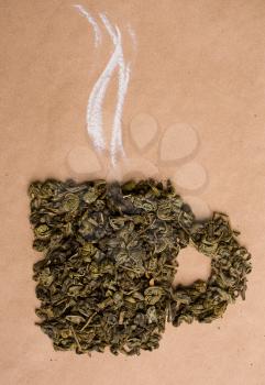 Dried green tea leaves are lined in the form of a cup on a beige background of kraft paper from above with chalk painted pairs