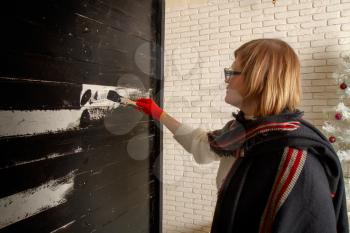 A woman in a small photo studio paints a wooden background with black paint