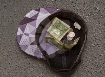 beggar's cap for milusty with coins and small bills on gray asphalt