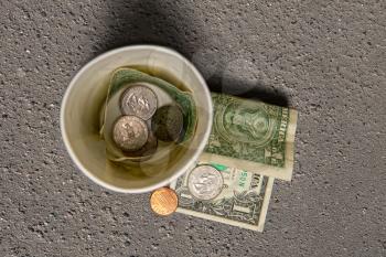 beggar's paper cup for millesti with coins and small bills on gray asphalt