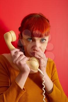 Pretty woman gossips by covering the receiver with an old telephone with a twisted wire against a bright red door