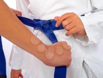 adult woman helps tighten the blue belt to the little girl karate
