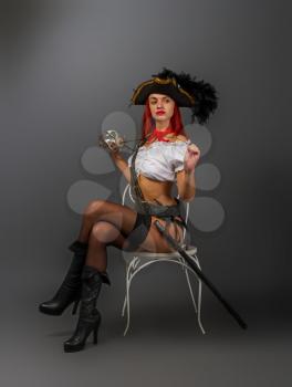 Bright armed sexy girl the pirate captain in a cocked hat is standing in underwear and stockings and a short white blouse is sitting on a chair.