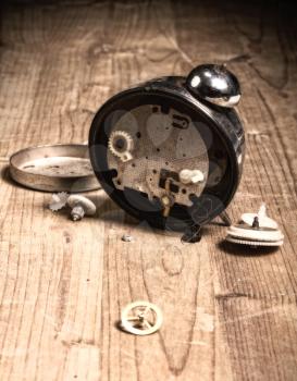 broken old analog alarm clock with loose parts and gears on a wooden surface