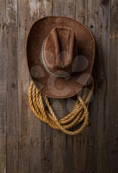 old classic wide-brimmed cowboy brown hat and lasso hanging on a rough wooden wall