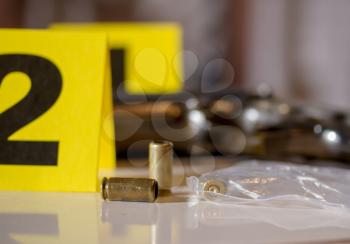 pistol cartridges scattered on the floor next to the crime scene weapons and yellow police markings with numbers near the evidence