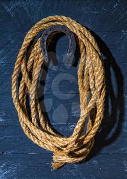 a steel horseshoe and a rough lasso rope hang on a dark wooden wall