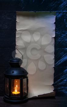 vintage vertical parchment on a dark wooden wall with place for your text and a lantern with a candle nearby