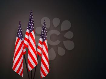 Three star-striped US flags on flagpoles on a dark background