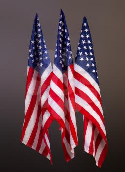 Three star-striped US flags on flagpoles on a gray background