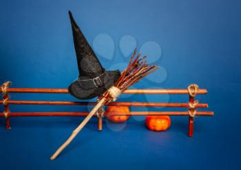 Classic witch black pointed hat and broom for flying near the fence with pumpkins