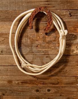Very rusty old horseshoe symbol of luck and lasso hanging on wooden wall close up