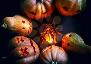 six halloween pumpkins gathered around a small fire in the dark