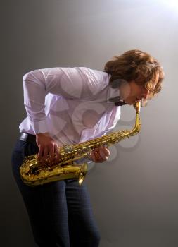 young saxophonist playing his bronze saxophone against a dark background