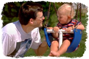 Royalty Free Photo of an Infant Child in a Baby Swing Observing Daddy Beside Him 