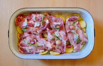 Raw pork neck chops with potatoes slices, rosemary and garlic in pan. The meal is prepared for baking.