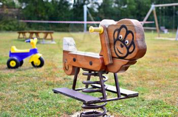 A close-up view of wooden swing on spring with plastic tricycle in the empty playground. Shallow depth of field. Focused on foreground.