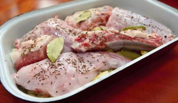Pieces of a uncooked seasoned rabbit and pork meat in a roasting pan.