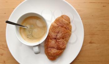 Breakfast with coffee and fresh croissant on a white plate.