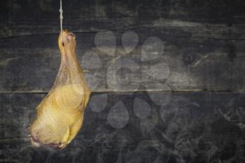 Smoked Chicken Leg Hanging on the Rope Against Wooden Background With Smoke