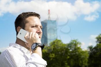 Successful Businessman Talking On The Phone In The Park With Corporate Office Building In The Background
