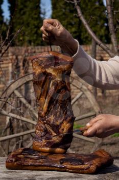Whole Smoked Bacon Slab Held By Woman's Hand While Being Sliced With Butcher's Knife In A Rustic Environment. Delicious Domestic Food