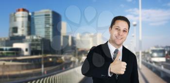 Businessman Smiling and Feeling Happy Giving Thumbs Up With Business City and Corporate Buildings In Background