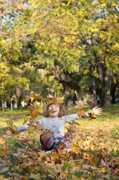 beautiful little girl throws autumn leaves