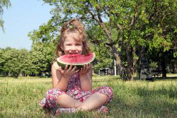little girl sitting on grass and eat watermelon