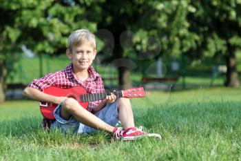 happy boy sitting on grass and play guitar