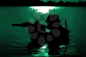 Silhouette of special forces with rifle in action during night raid crossing river in the jungle waist deep in the water. Moon path glowing