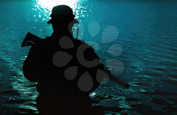 Silhouette of special forces with rifle in action during river raid in the jungle waist deep in the water. Front view, half length