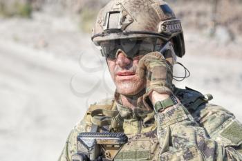 Closeup shot of soldier calliong phone in the desert among rocks
