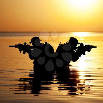 Army soldiers with rifles orange sunset silhouette in action during raid crossing river in the water