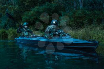 Special forces men with painted faces in camouflage uniforms paddling army kayak. Boat moving calmly across the river, diversionary mission, twilight