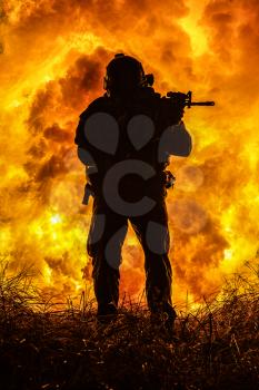 Backlit silhouette of special forces marine operator in forest on fire explosion background. Battle, bombs exploding, fighting no matter what