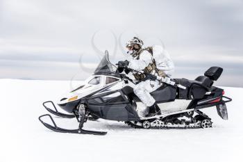 Army soldier in winter camo somewhere in the Arctic moving across the snow field riding tracked snowmobile