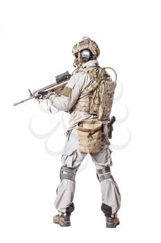 Army soldier in Protective Combat Uniform holding Special Operations Forces Combat Assault Rifle. Knee pads, mag recovery pouch, chest rig, military boots. Studio shot, isolated on white, back view