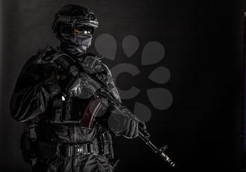 Police special forces, quick reaction team officer, tactical group fighter in black uniforms, helmet and hidden behind mask identity, armed with assault rifle, low key studio shoot on black background