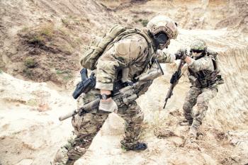 US ranger, modern infantryman, special reconnaissance team member or military scout in ammunition, armed with service rifle helping brother in arms to climb on sand dune. Army brotherhood and teamwork