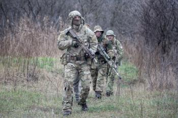 Special operations forces soldiers, elite troops tactical group, infantry fighters in combat uniforms, armed service and sniper rifles, marching in line behind commander, leader in forest or bush