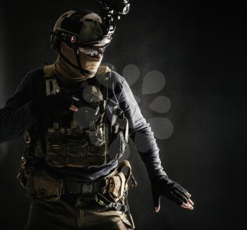 Special operations fighter in helmet with night-vision, thermal imaging device, load carrier carefully moving with caution in darkness, holding hand on pistol, ready for fight during dangerous mission