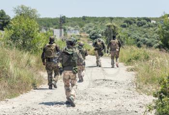 Army soldiers team, special operations infantrymen loaded with ammunition and weapon, walking on country road in woodland. Commando reconnaissance team patrolling, moving to mission destination point