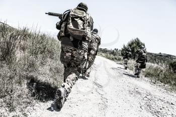 Army soldiers team in combat uniform, load carriers and helmets running on countryside road, aiming guns and sneaking in bush. Special forces infantrymen group moving with cautious at abandoned area