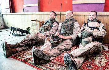 United States marines in camouflage uniform and ammunition sitting on floor at combat outpost or temporary base on mission, talking in relaxing atmosphere, resting after hard day on military service